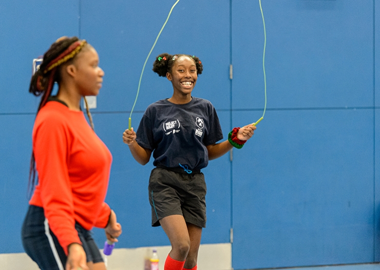 A girls uses a skipping rope in a sports hall and smiles at the camera