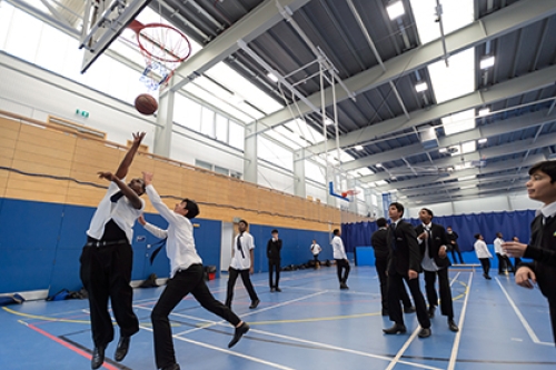 A group of schoolboys play basketball indoors