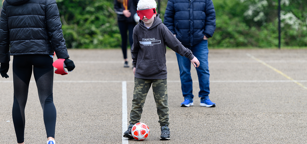 A boy wearing a blindfold tries blind football in a playground