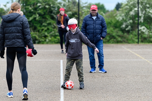 A boy wearing a blindfold tries blind football in a playground