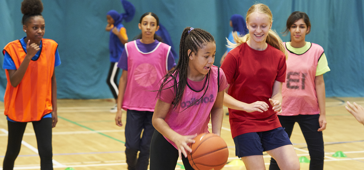 A group of girls play basketball in a sports hall