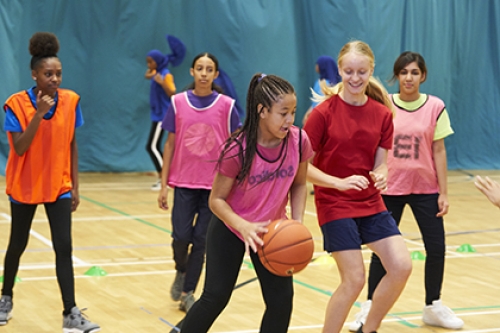 A group of young girls play basketball in a sports hall