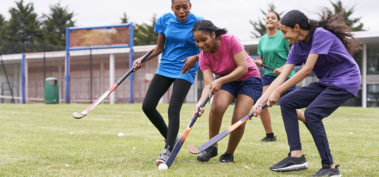 Four girls play hockey on a school field