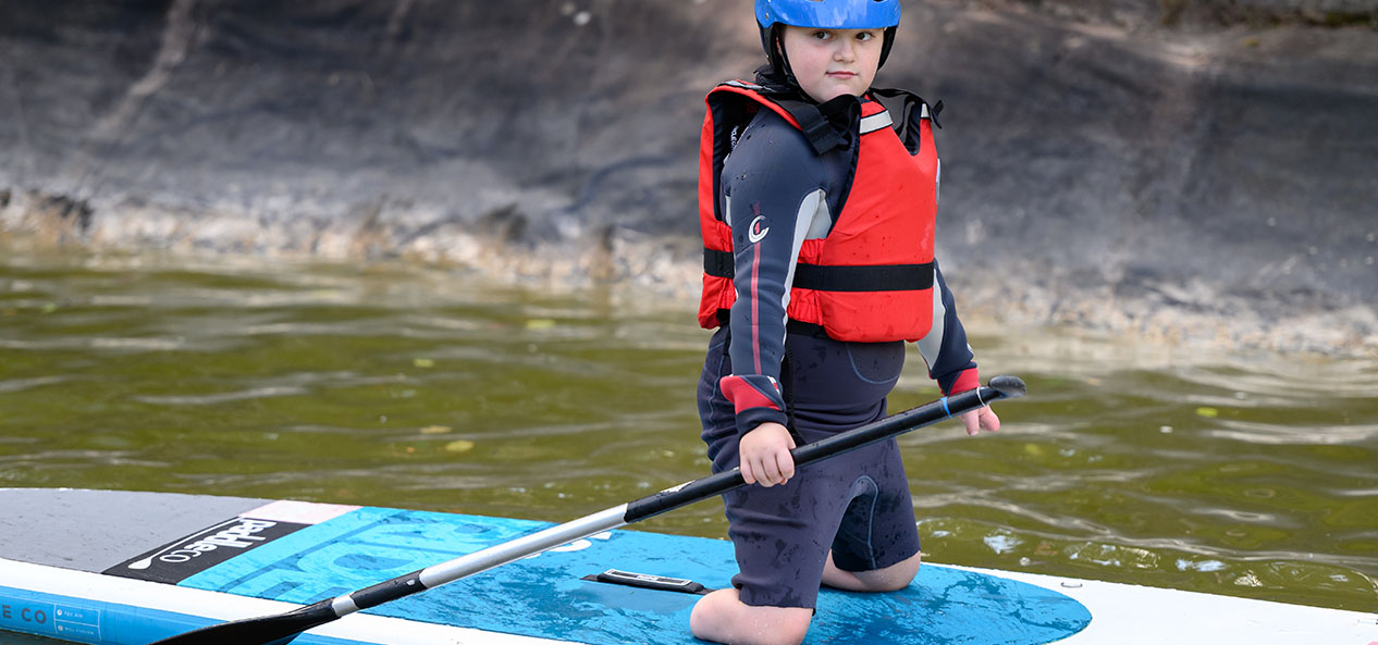 A double amputee-of-the-legs boy, kneels on a paddle board