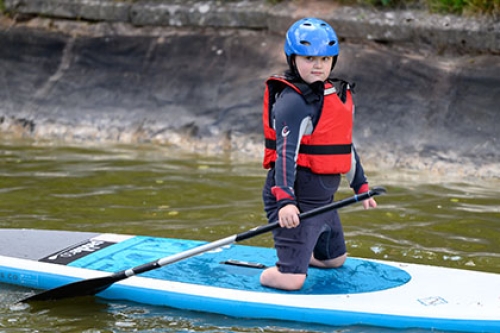 A double amputee-of-the-legs boy, kneels on a paddle board