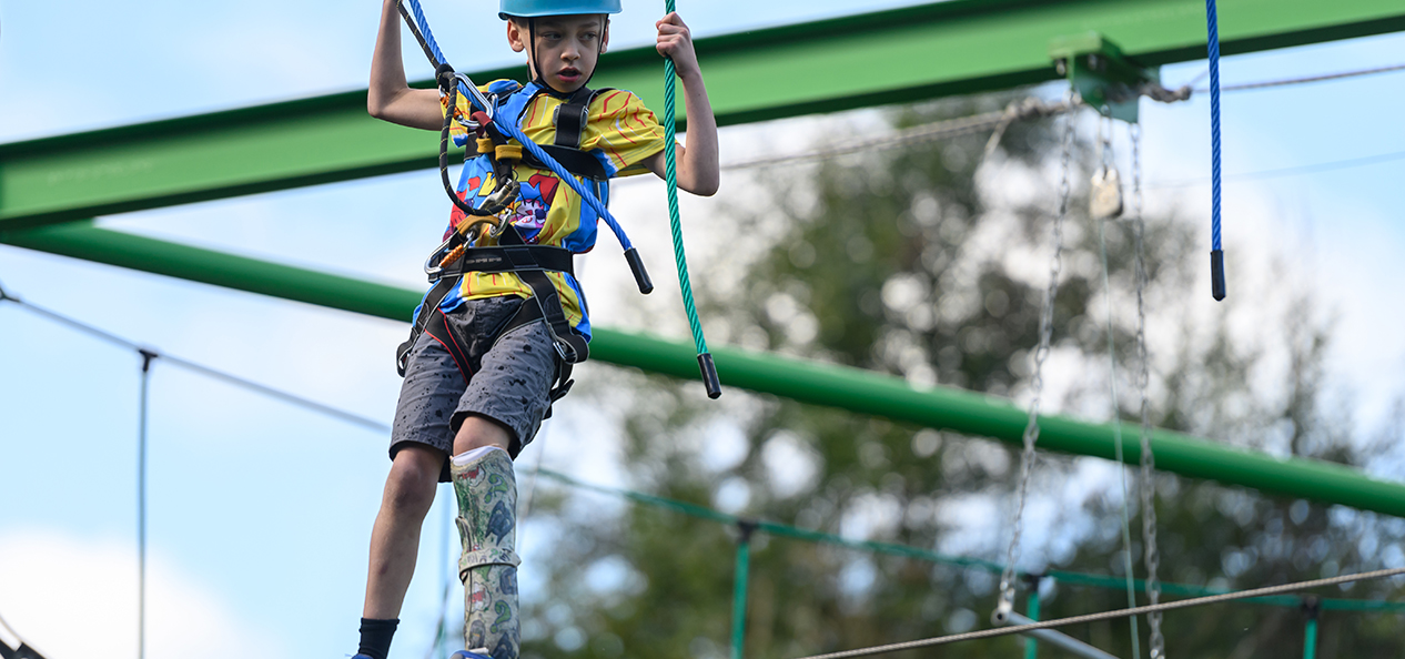 A boy with a prosthetic leg balances on a high ropes course.