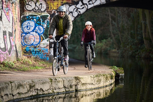 A man and a woman cycle on a canal towpath