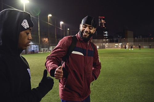 Two men fist-bump as they walk onto a 4G pitch to play football