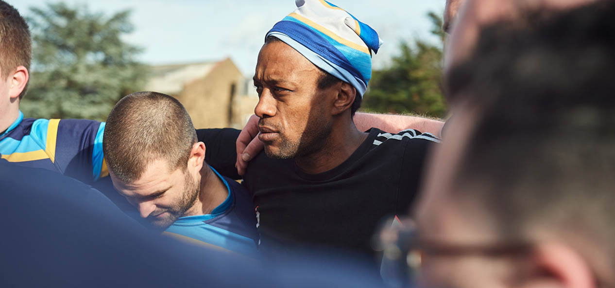 A man embraces his teammates while in a meeting during an outdoors rugby game.