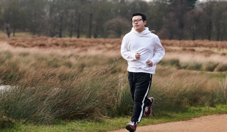 A man jogs on a path in a large area of parkland.