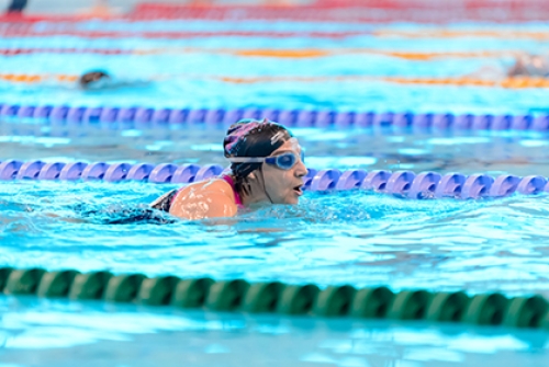 A woman wearing goggles and a swimming hat swims lengths in a pool