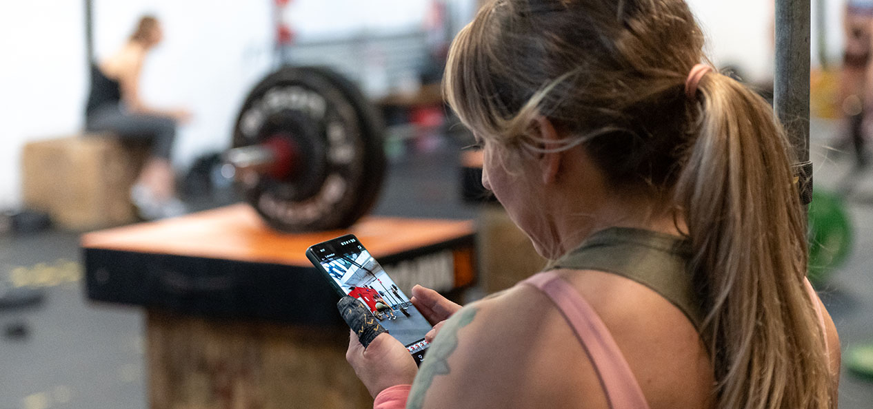 A woman checks her phone during a weighlight session in an indoors gym