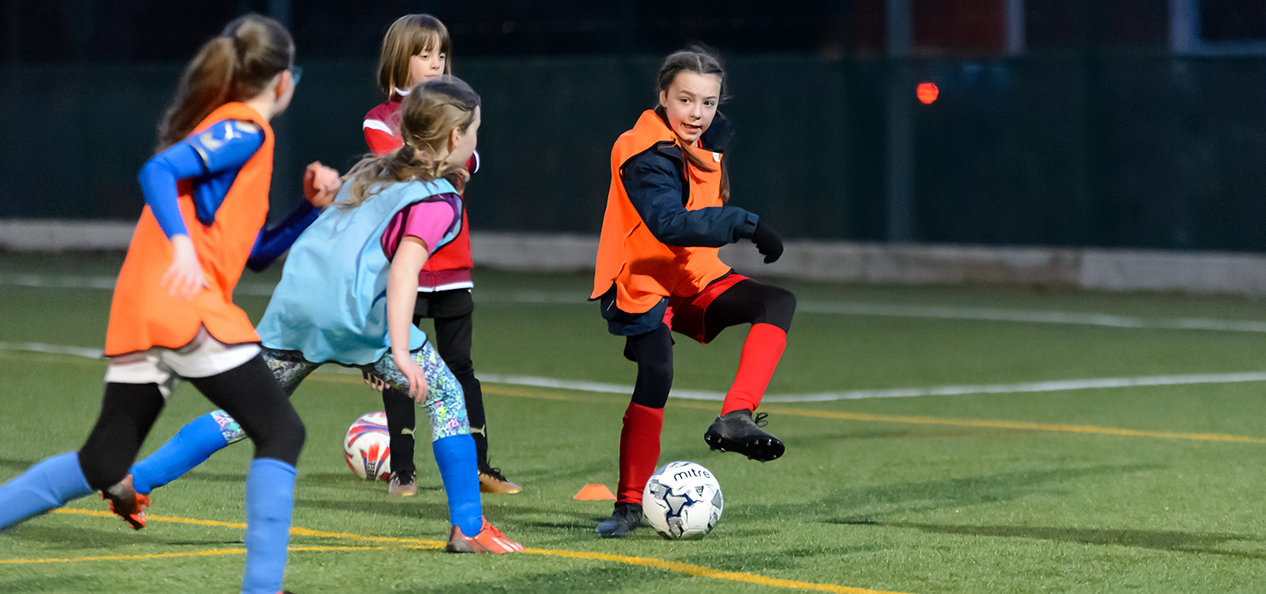 A group of girls play football on an artificial pitch.