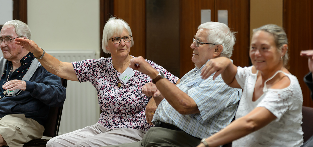 A group of older adults participate in seated exercise in a community centre