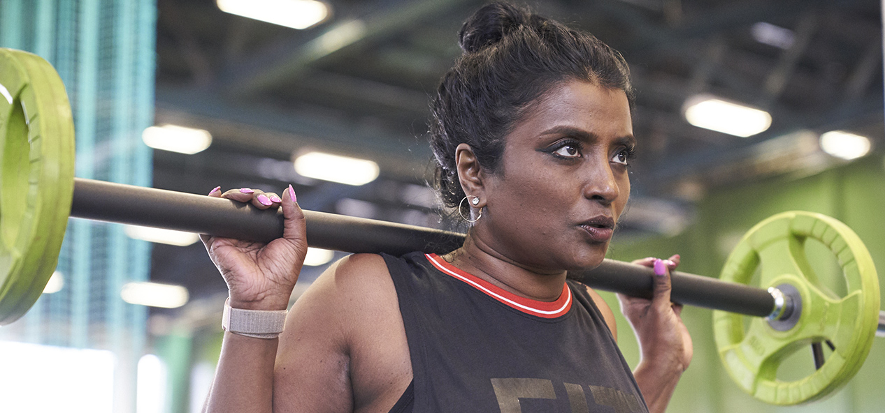 A woman squats using a barbell in a gym