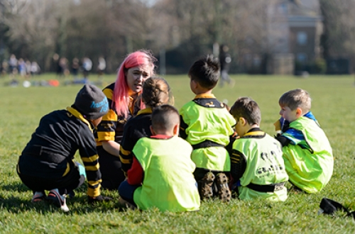 A female rugby coach crouched down with a group of children.