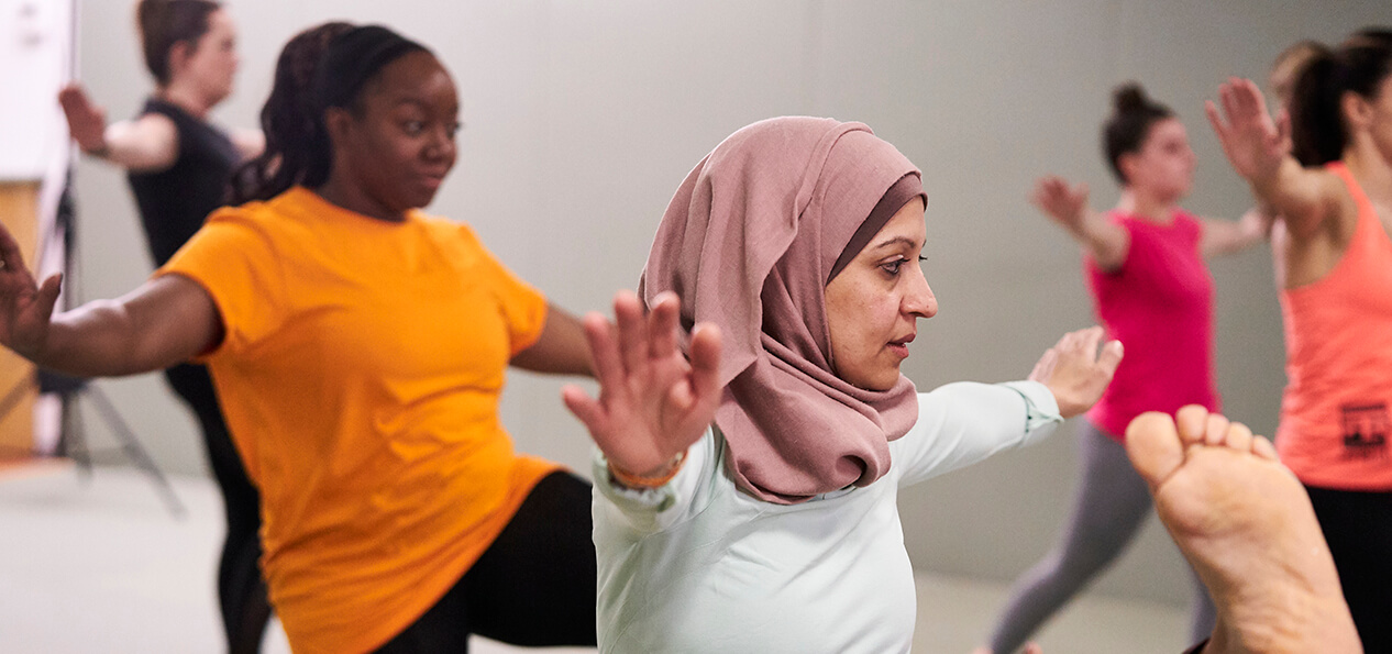 A group of women doing some balance exercises in an indoor hall.