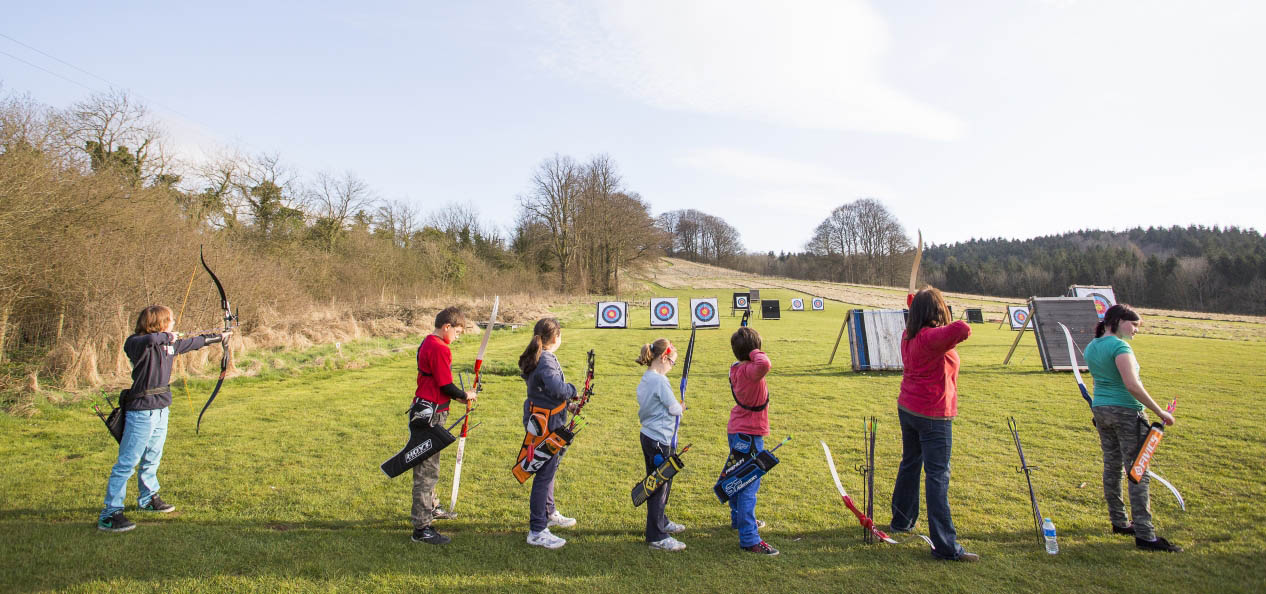 A group of young people aiming their arrows during an archery session.