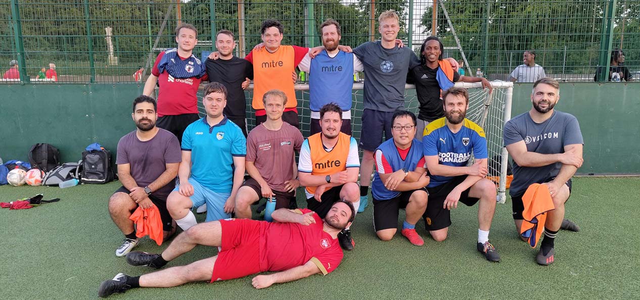 Team members of the Barnes Stormers FC pose together for a team picture on an outdoors football pitch.