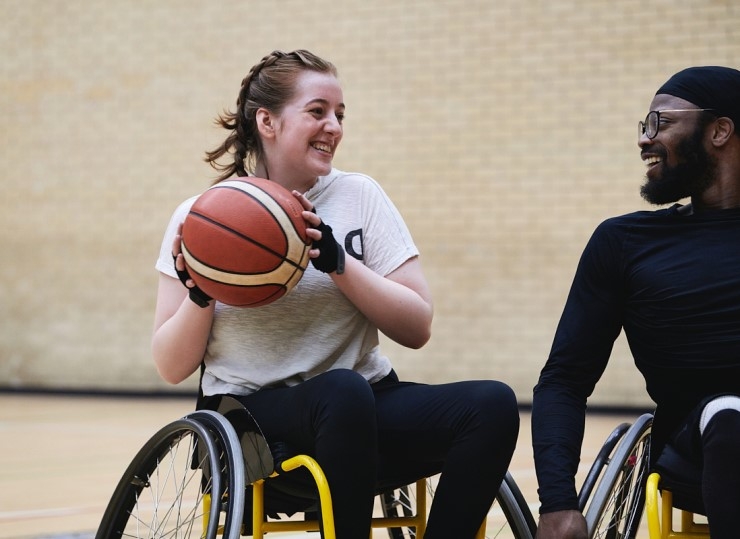 A female player holding a ball smiles during a game of wheelchair basketball, with a male player next to her