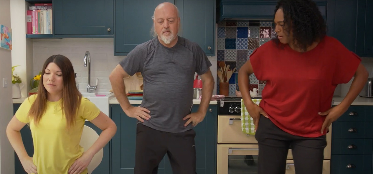 Bill Bailey, an instructor and a woman with arthritis, perform hip circles in a kitchen