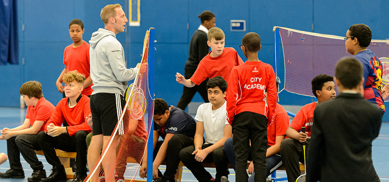 A PE teacher and children inside a sports hall.