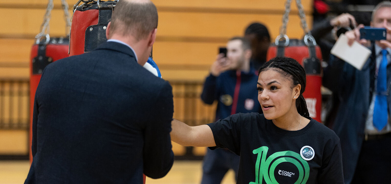 A woman is boxing with Prince William on an indoors sports centre