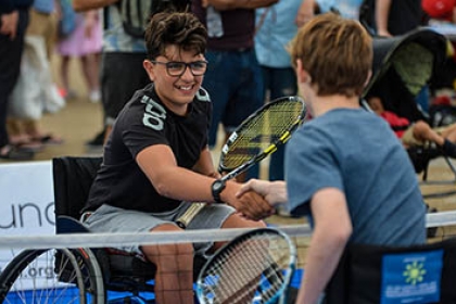 Two boys playing wheelchair tennis shake hands at the net