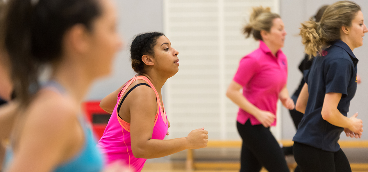 A group of women train for netball in an indoor hall.