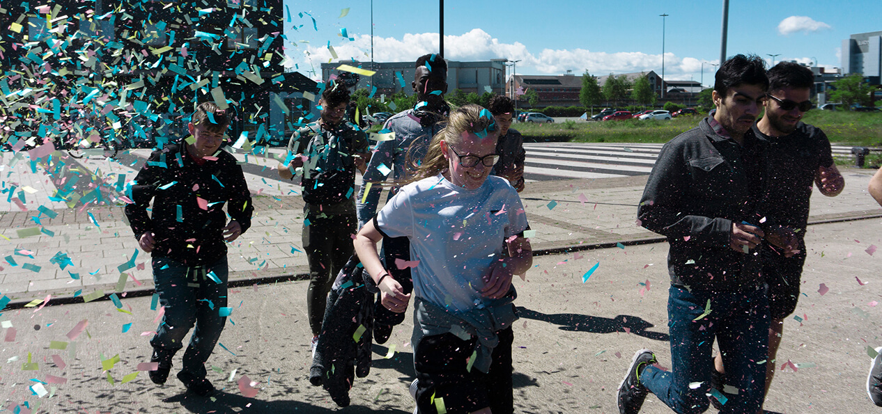 A group of schoolchildren smiling as they run through falling confetti.