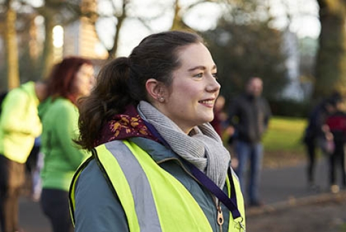 A female volunteer at a parkrun event, with a high-vis vest on and a whistle round her neck