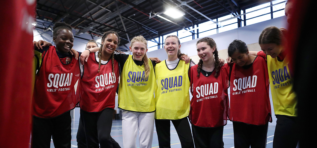 A group of teenage girls gather in a huddle at an indoor football session