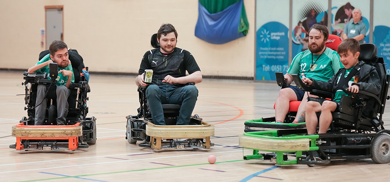 A group of young men and boys on wheelchair play Power Hockey indoors. 