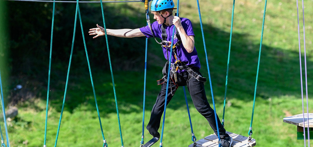 A man with a prosthetic leg walks across a high ropes course.