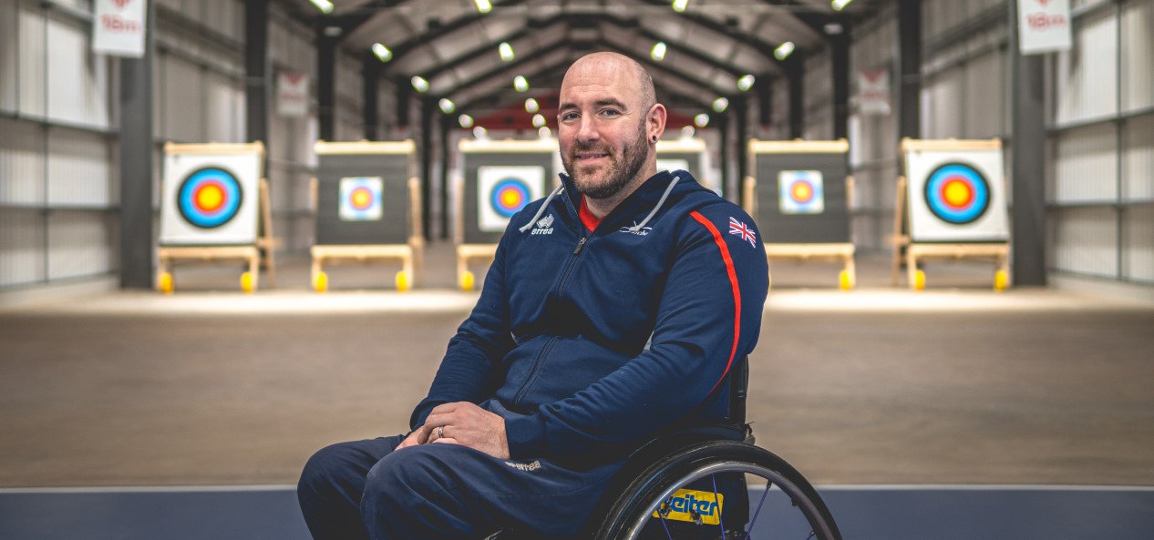 Paralympian archer Nathan Macqueen poses for a photo at the Performance Archery Centre in Lilleshall, with targets behind him..