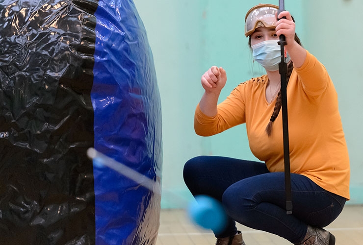 A teenage girl crouches down as she fires a foam arrow in a sports hall