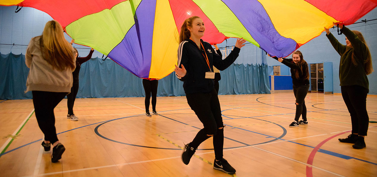 A group of teenage girls playing under a rainbow sheet