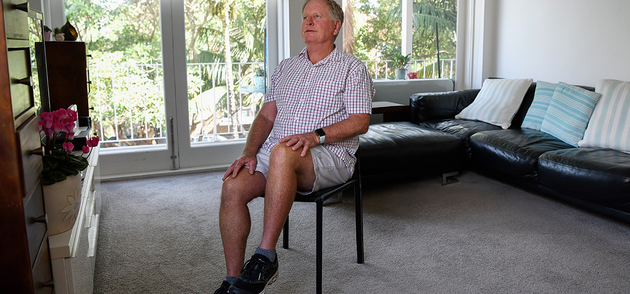 An older man performs seated exercises in his home.