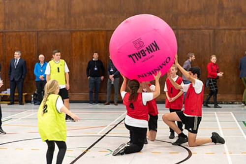 A group of people play with a giant ball on an indoors hall.