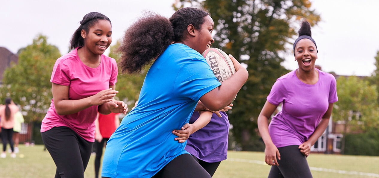 A girl runs with a rugby ball as three other players follow her.