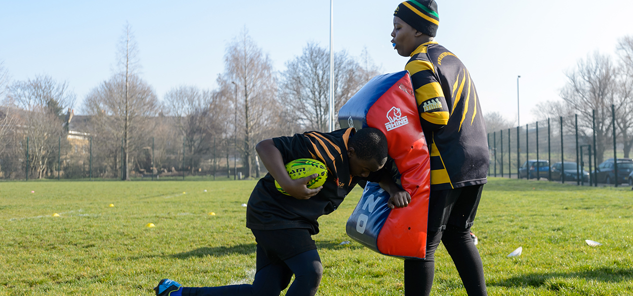 Two rugby players perform a tackling drill with one holding a tackling pad