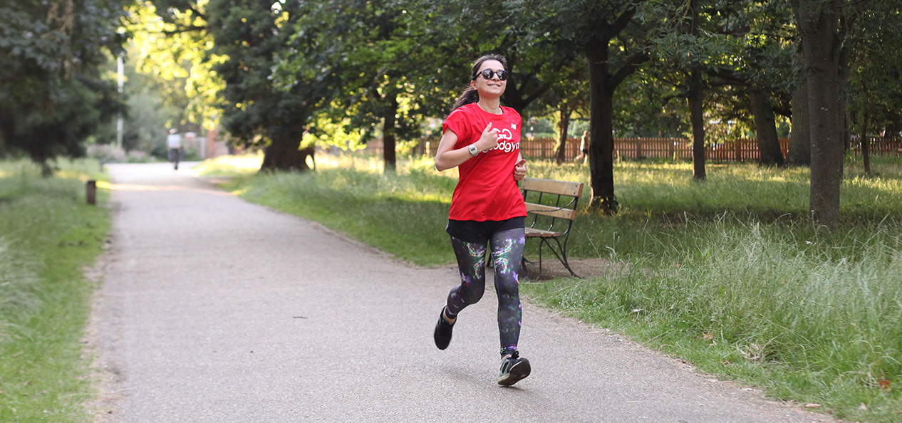 A woman runs alone in a park, wearing a Good Gym t-shirt