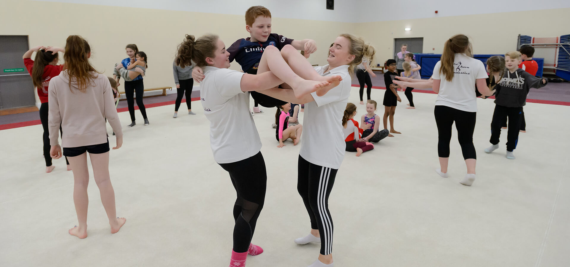 Two girls lifting young boy in sports hall