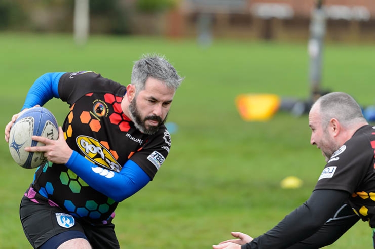 A man carrying a rugby ball tries to evade being tackled