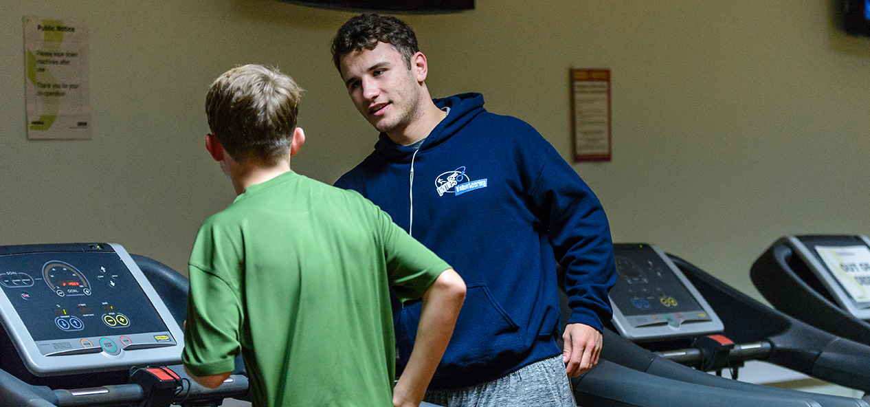 A Street Games volunteer instructs a boy how to use a treadmill