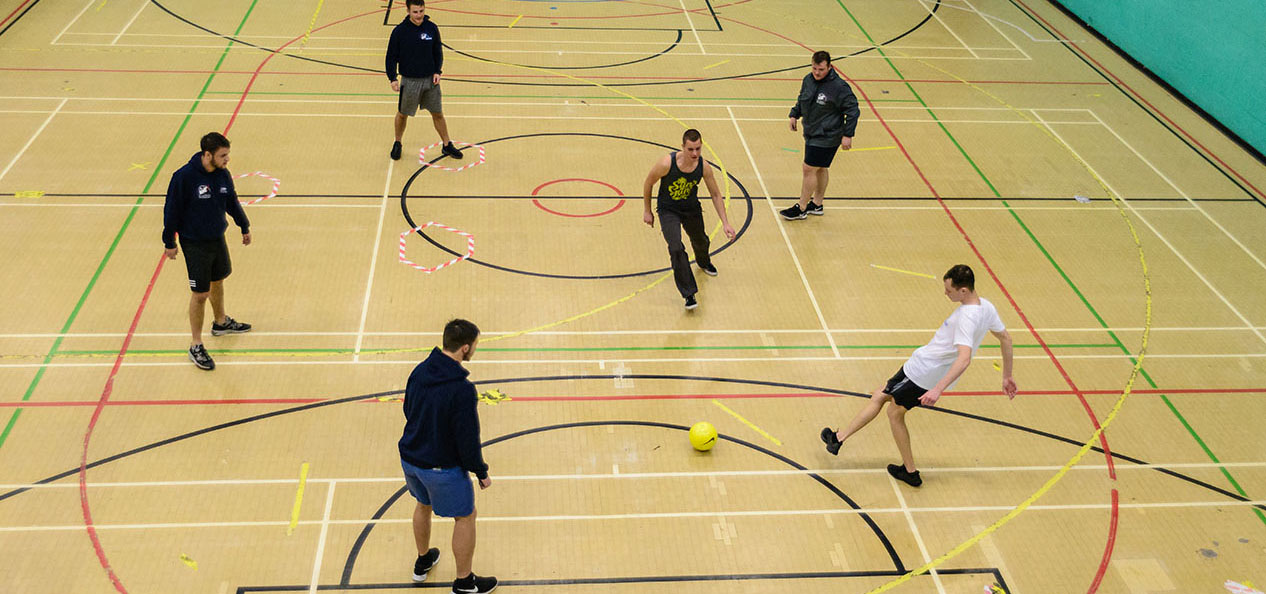 Overhead shot of a group of group of men kicking a football around a sports hall