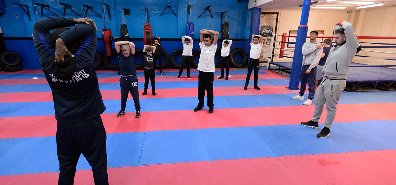 A group of people stretching as part of a warm up in a boxing hall.