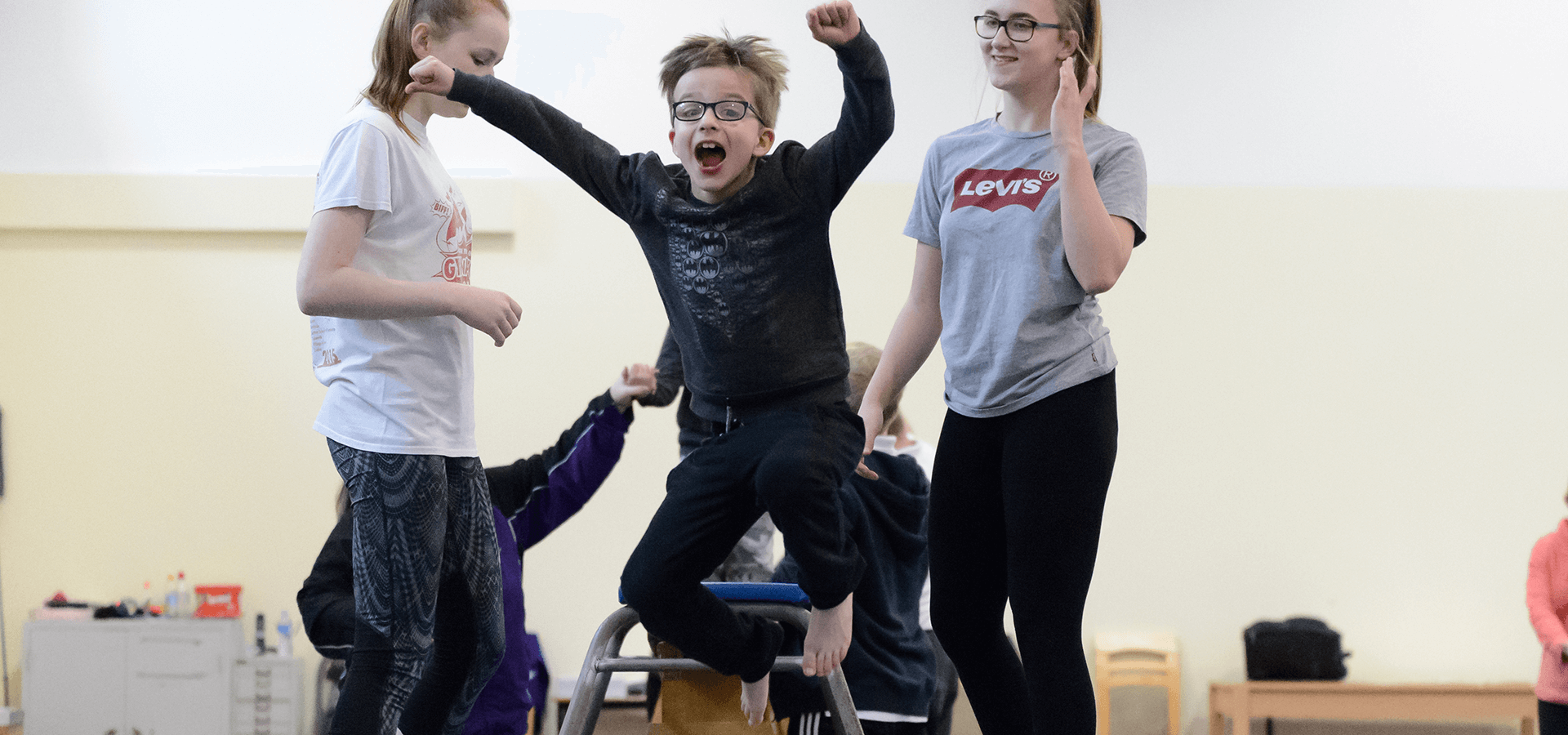 Boy jumping on small trampoline with two girls helping